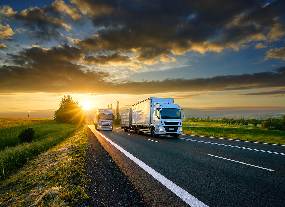 Insurance Solutions - Small Truck Overtakes Heavy Truck on the Asphalt Road in Rural Landscape at Sunset