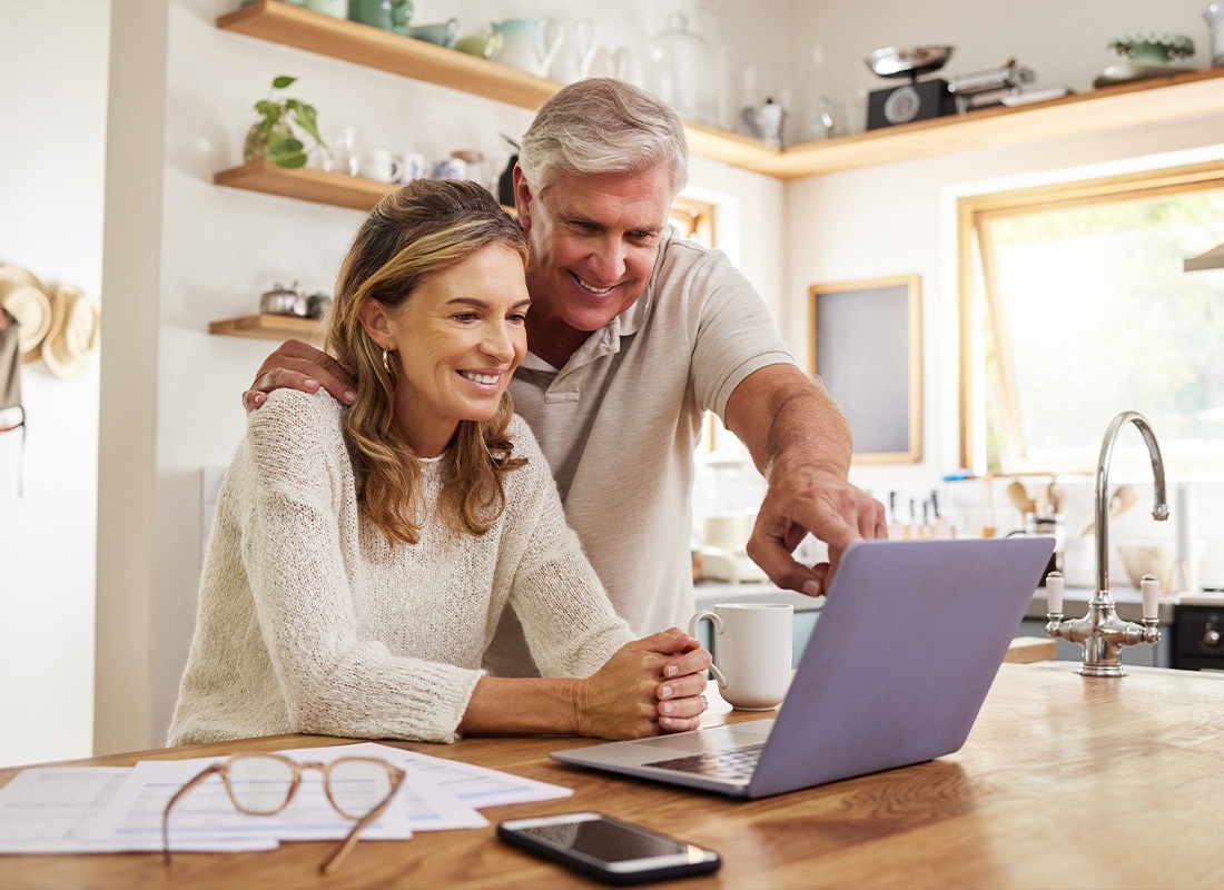 Service Center - Middle Aged Couple Smiling While Looking at a Laptop Sitting on a Wooden Table